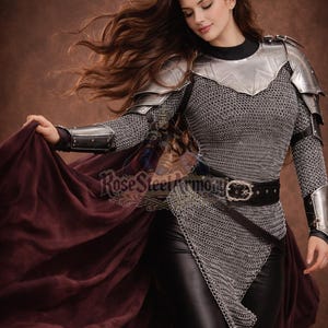 May include: A woman's medieval-style armor set. The armor includes a silver metal chest plate, shoulder guards, and chainmail. The model is wearing black leather pants and a black belt. A burgundy cape is draped over the arm. The text "Rose Steel Armory" is visible.