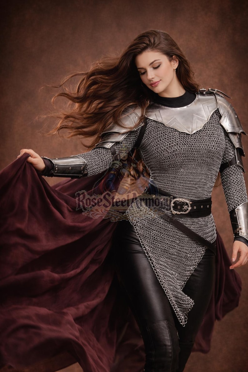 May include: A woman's medieval-style armor set. The armor includes a silver metal chest plate, shoulder guards, and chainmail. The model is wearing black leather pants and a black belt. A burgundy cape is draped over the arm. The text "Rose Steel Armory" is visible.