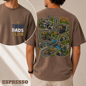 May include: Espresso-colored t-shirt with the text "TIRED DADS CLUB" and a police badge graphic on the front. The back features a detailed map illustration of a police adventure, including buildings, roads, and police cars.