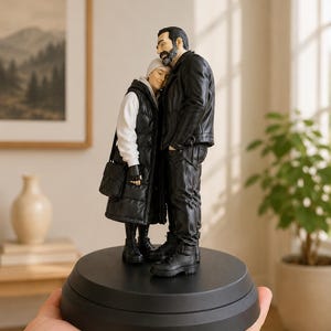Peut inclure: Une figurine détaillée représentant deux personnages debout ensemble sur une base noire circulaire. L'un porte une veste et un pantalon en cuir noir avec des bottes noires, tandis que l'autre porte un sweat à capuche blanc, une longue doudoune noire.