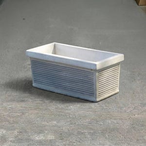 May include: A rectangular off-white planter with a smooth top rim and horizontal ribbed detailing along the sides. The container features a clean, structured design with a wide opening and a solid base, presenting a neutral color and texture.