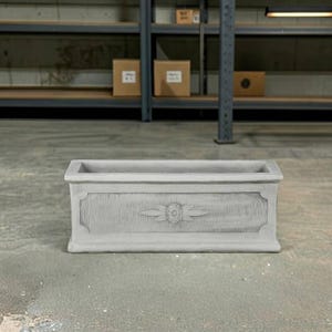 May include: A rectangular light gray concrete planter featuring a decorative central floral motif. The exterior surface displays a textured panel design with a raised border, providing a structured appearance for this functional garden container.