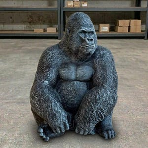 May include: A seated gorilla statue with a textured, dark gray finish. The gorilla is depicted with a serious expression, muscular chest, and detailed fur-like texture. The statue is sitting on a concrete floor.