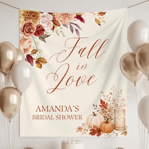 May include: A cream-colored fabric backdrop featuring the text Fall in Love and AMANDA'S BRIDAL SHOWER in brown script and block letters. The design includes watercolor illustrations of autumn flowers, leaves, pumpkins, and a candle.