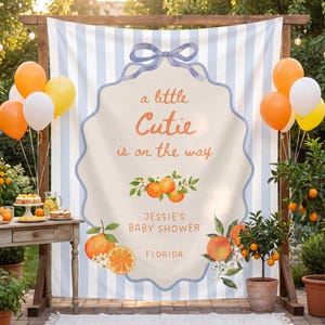 Puede incluir: Un telón de fondo para baby shower con un diseño de rayas azules y blancas. El telón de fondo presenta el texto "a little Cutie is on the way" y "Jessie's Baby Shower Florida". Globos naranjas, amarillos y blancos están atados al marco de madera.