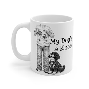 Peut inclure: Un mug en céramique blanc avec une illustration en noir et blanc représentant une personne portant un t-shirt couvert d'empreintes de pattes boueuses, debout à côté d'un chien aux poils bouclés. Le texte "My Dog's a Knob" est imprimé en noir.