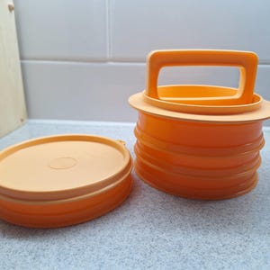 Peut inclure: Conteneur en plastique orange avec une poignée et un couvercle séparé. Le conteneur a une base ronde et une poignée sur le dessus. Le couvercle est également rond et s'adapte parfaitement au conteneur. Le conteneur est en plastique durable.