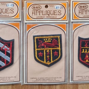May include: Three vintage So-Rite appliqués on cards. Each appliqué is a shield design with embroidered details in red, black, gold, and silver. The cards read "APPLIQUES LAVABLE - WASHABLE".
