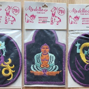 May include: Embroidered appliques with a black background and purple trim. One applique features a seated figure, while others have a stylized design in yellow, teal, and purple. Each applique is packaged with a Modella trade mark tag.