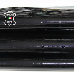 May include: Close-up of black leather with a glossy finish. The leather is folded in thirds, revealing the texture of the material. The leather is labeled "ITALIAN SKINS".