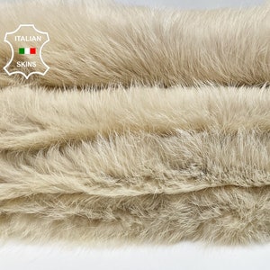 May include: Close-up of a light beige fur fabric. The fur is soft and fluffy, with a subtle sheen. The fabric is folded in thirds, showing the texture and depth of the fur.