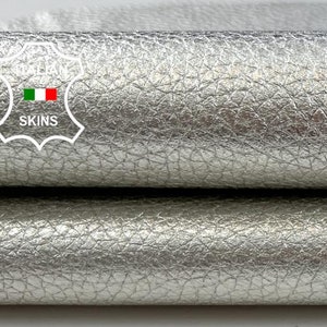 Puede incluir: Primer plano de dos piezas de cuero metálico plateado. El cuero tiene una superficie texturizada.