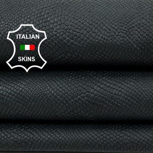 Op de afbeelding: Close-up van gevouwen zwart leer met een getextureerd, reptielachtig patroon. Het leer is in drie lagen gestapeld, wat de flexibiliteit en diepte laat zien. Het Italian Skins-logo is zichtbaar.