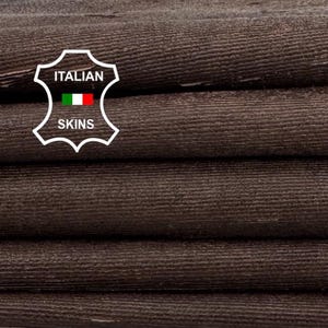 May include: A stack of folded, dark brown leather hides. The leather has a textured surface and appears to be of high quality. The image includes a logo that says "Italian Skins". The hides are stacked on a white surface.