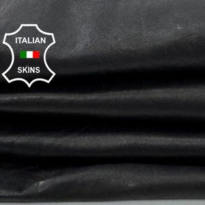 May include: Close-up of folded black leather. The leather has a textured appearance and is stacked in layers. The image includes a logo with the text "ITALIAN SKINS" and an Italian flag.