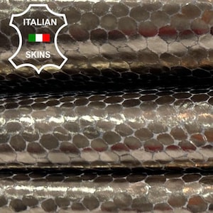 Puede incluir: Primer plano de tres piezas de cuero de serpiente plateado metálico. El cuero tiene un patrón hexagonal y un acabado brillante. El texto "ITALIAN SKINS" es visible en la esquina superior izquierda.