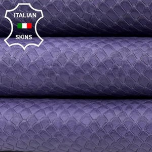 Peut inclure: Gros plan sur des feuilles de cuir violettes texturées empilées. Le cuir présente un motif en écailles et un léger éclat. Le logo Italian Skins est visible dans le coin supérieur gauche. Les feuilles sont empilées sur une surface blanche.