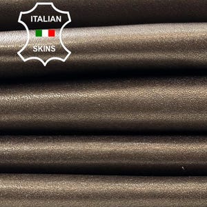 May include: Close-up of stacked sheets of brown leather. The leather has a smooth, slightly textured surface. The image shows several layers of the material, highlighting its texture and color. The leather is a neutral brown tone.