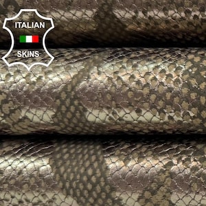 May include: Close-up of three rolls of metallic, snakeskin-textured leather. The leather has a silver and bronze color scheme with a scale pattern. The rolls are stacked on top of each other.