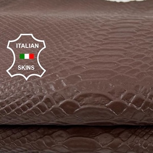 May include: A folded piece of dark brown leather with a textured snake skin pattern. A white shield-shaped logo is visible on the left side with the text ITALIAN SKINS and a small Italian flag icon printed inside the emblem.