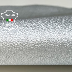 May include: Close-up of a silver leather material with a textured surface. The leather is rolled up and the label "ITALIAN SKINS" is visible in the top left corner.