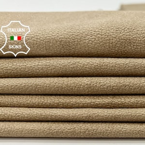 Puede incluir: Primer plano de una pila de piezas de cuero beige. El cuero tiene una superficie texturizada.