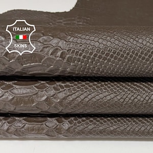 May include: Close-up of a stack of brown snakeskin leather. The leather has a textured, scaly surface. The label "ITALIAN SKINS" is visible in the top left corner.