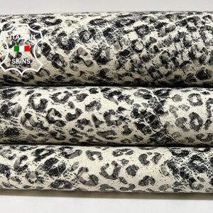 Könnte beinhalten: Nahaufnahme von drei Rollen weißem Leder mit schwarzem Leopardenmuster. Das Leder ist strukturiert und hat einen leicht abgenutzten Look.