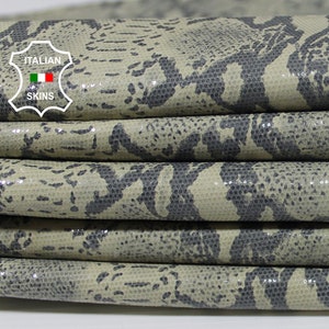 May include: Close-up of a stack of beige snakeskin leather with a dark gray pattern. The leather is folded in a circle, showing the texture and detail of the material. The label "ITALIAN SKINS" is visible in the top left corner.