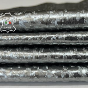 May include: Close-up of a stack of silver leather with a textured, embossed pattern. The leather has a metallic sheen and is folded in a stack.
