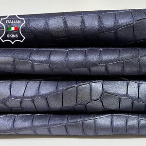 May include: Four pieces of dark blue crocodile embossed leather stacked on top of each other. The leather has a subtle sheen and a textured surface.