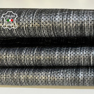 May include: Close-up of three rolls of black perforated leather with white stitching. The leather has a textured surface and is ideal for crafting projects.