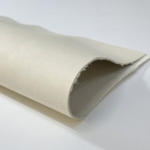 May include: A close-up of a white leather sheet, rolled up and showing the texture of the leather. The sheet is labeled "ITALIAN SKINS" with an Italian flag.