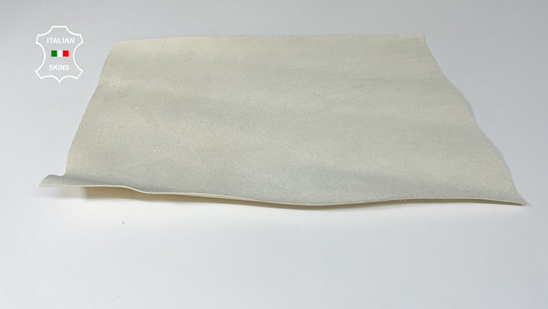 K&ouml;nnte beinhalten: Nahaufnahme eines St&uuml;cks cremefarbenen Leders. Das Leder ist glatt und hat einen leichten Glanz. Es liegt flach auf einer wei&szlig;en Oberfl&auml;che.