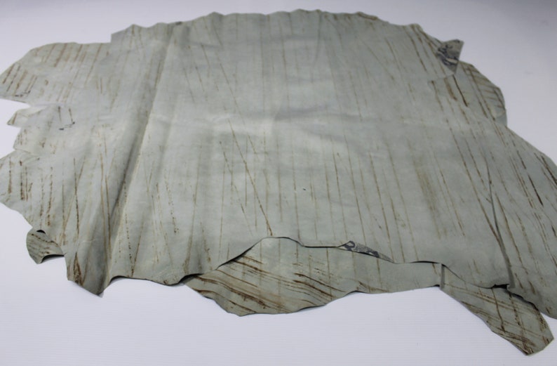 May include: A light gray leather hide with a textured surface. The leather has a natural, rustic look with visible lines and markings.