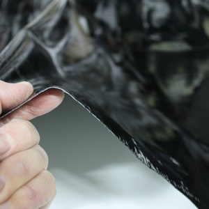 May include: A close-up of a black, flexible material with a textured surface. The material is being held by a hand, showing its flexibility.