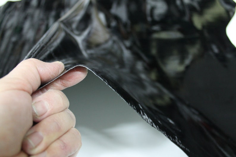 May include: A close-up of a black, flexible material with a textured surface. The material is being held by a hand, showing its flexibility.