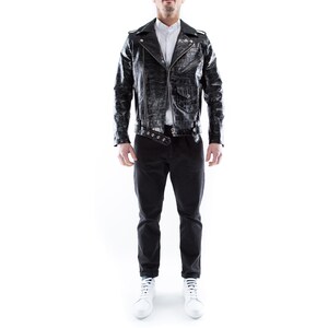 May include: A black leather jacket with a zipper closure and a white collared shirt underneath. The jacket has a crocodile-embossed pattern and a belt with silver buckles. The person is wearing black pants and white sneakers.