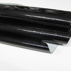 May include: Black faux leather with a crocodile embossed pattern. The leather is folded in thirds and has a glossy finish.