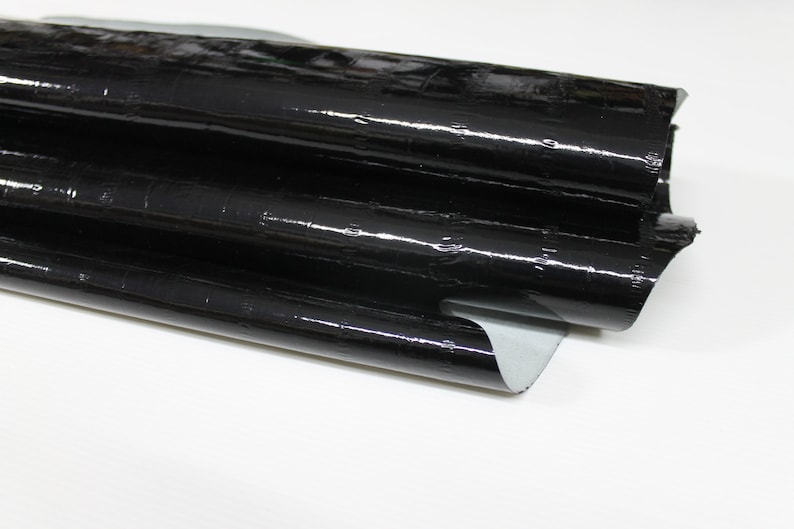 May include: Black faux leather with a crocodile embossed pattern. The leather is folded in thirds and has a glossy finish.