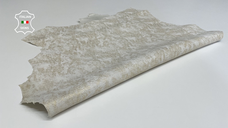 May include: A piece of off-white leather with a subtle gold flecked pattern. The leather is folded in half and has a rough, textured surface.