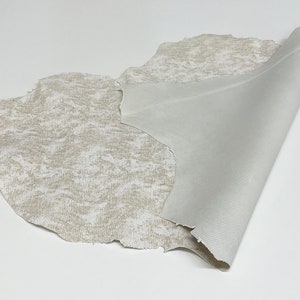 May include: A piece of off-white leather with a textured surface. The leather is folded over to show the smooth underside.