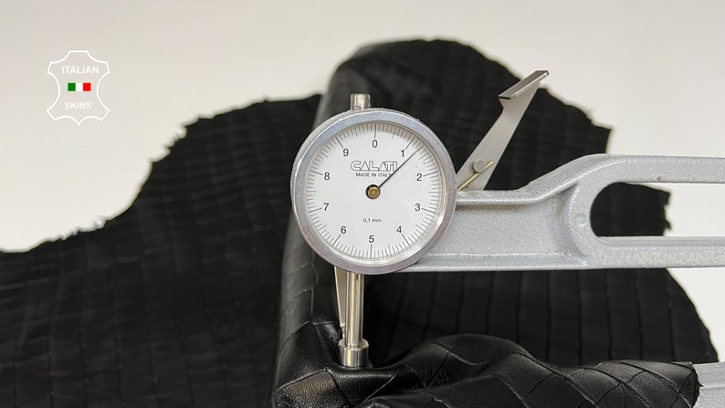 May include: A close-up of a leather sample being measured with a dial gauge. The gauge reads 3.1 mm. The leather is black and has a textured surface.