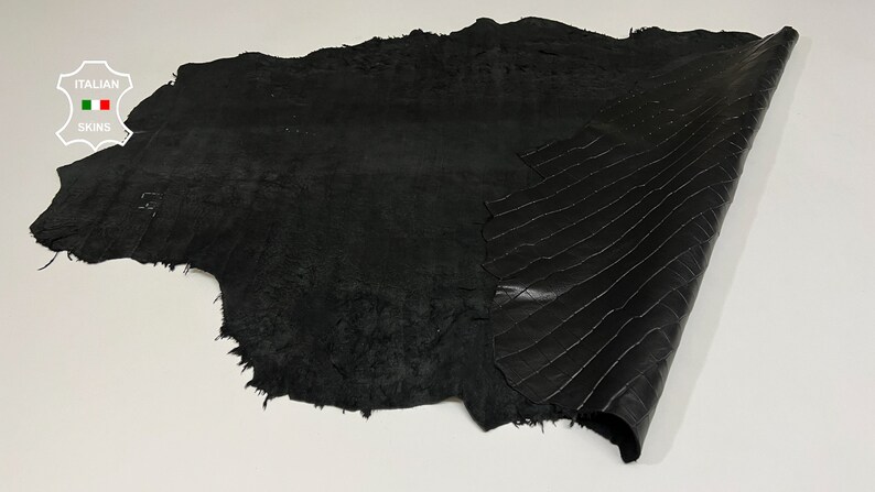 May include: Black leather hide with a textured surface. The leather is folded in half, revealing a smooth, patterned side.