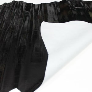 May include: Black leather with a textured, embossed pattern. The leather is folded over to reveal a white backing.