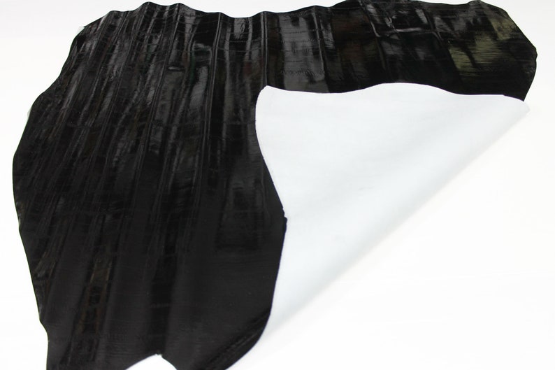 May include: Black leather with a textured, embossed pattern. The leather is folded over to reveal a white backing.