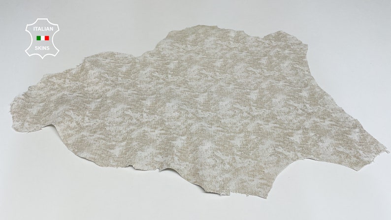 May include: A piece of off-white leather with a mottled, textured surface. The leather is slightly wrinkled and has a natural, organic look.