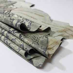 May include: A stack of light green and brown patterned leather hides. The leather has a textured surface and a subtle sheen.