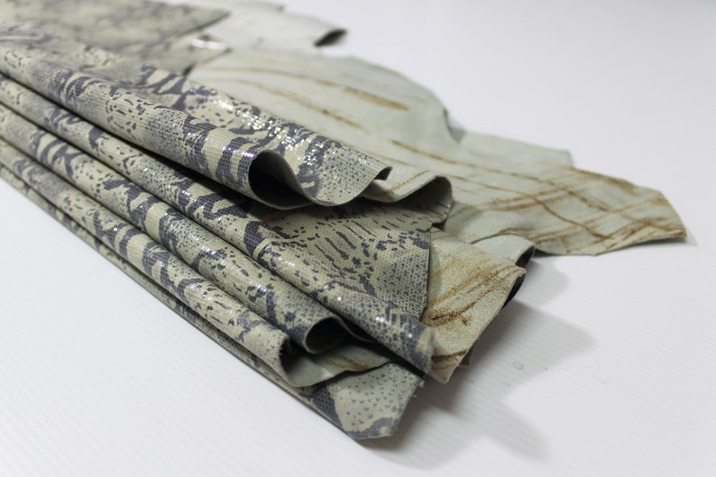 May include: A stack of light green and brown patterned leather hides. The leather has a textured surface and a subtle sheen.