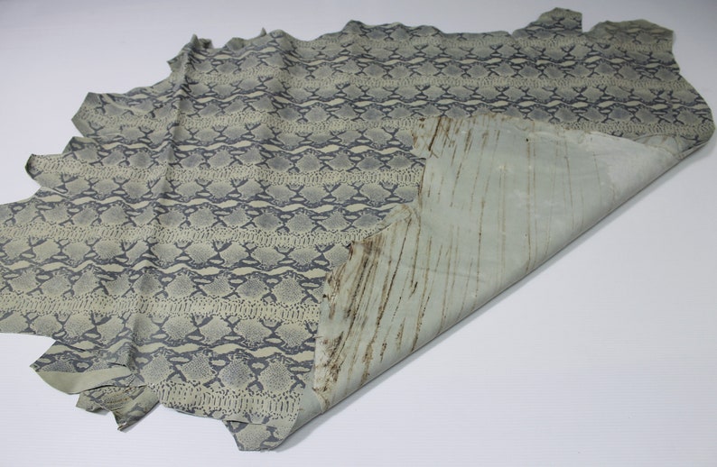 May include: A light green snakeskin leather hide with a dark gray pattern. The hide is folded in half, revealing the underside of the leather.